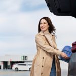 Femeie care așază o valiză albastră în portbagajul unei mașini, imagine ilustrativă pentru servicii rent a car la Aeroportul Iași.
